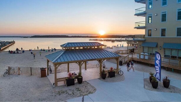 Ein Strandhotel mit überdachter Veranda, einem Steg und Blick auf den Sonnenuntergang über dem Wasser.