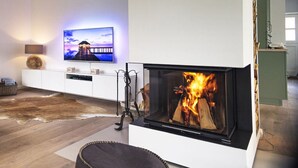 Ett modernt vardagsrum med en öppen spis, en platt-TV som är monterad på väggen och ett trägolv.