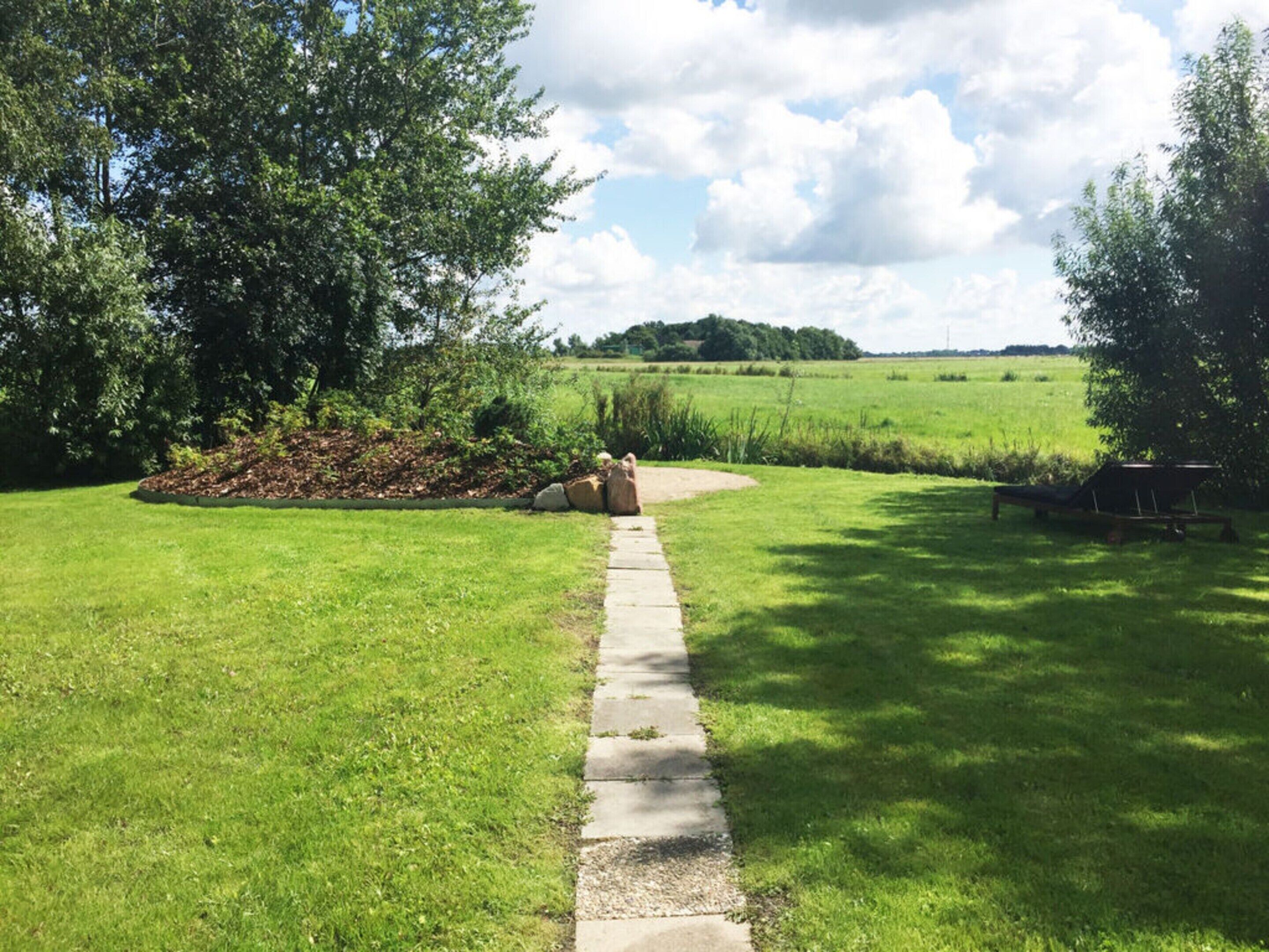 A pathway leading through a grassy area with a bench and a tree on the right.