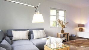 Ett modernt vardagsrum med en grå hörnsoffa, ett soffbord i glas, ett sidobord i trä med en vas och ett vitt skåp.