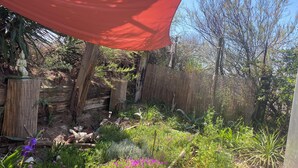 A garden with a variety of plants, a wooden fence, and a red canopy. - Atypical, set on the beach with direct access, swimming pool, barbecue, pets allowed (Marseillan)