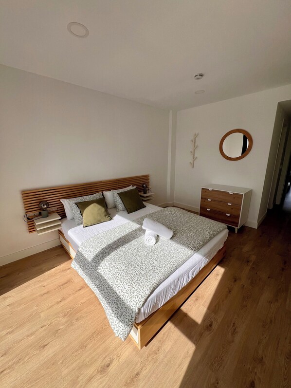 Un dormitorio con una cama de madera, una mesita de noche, un aparador y un espejo en la pared.