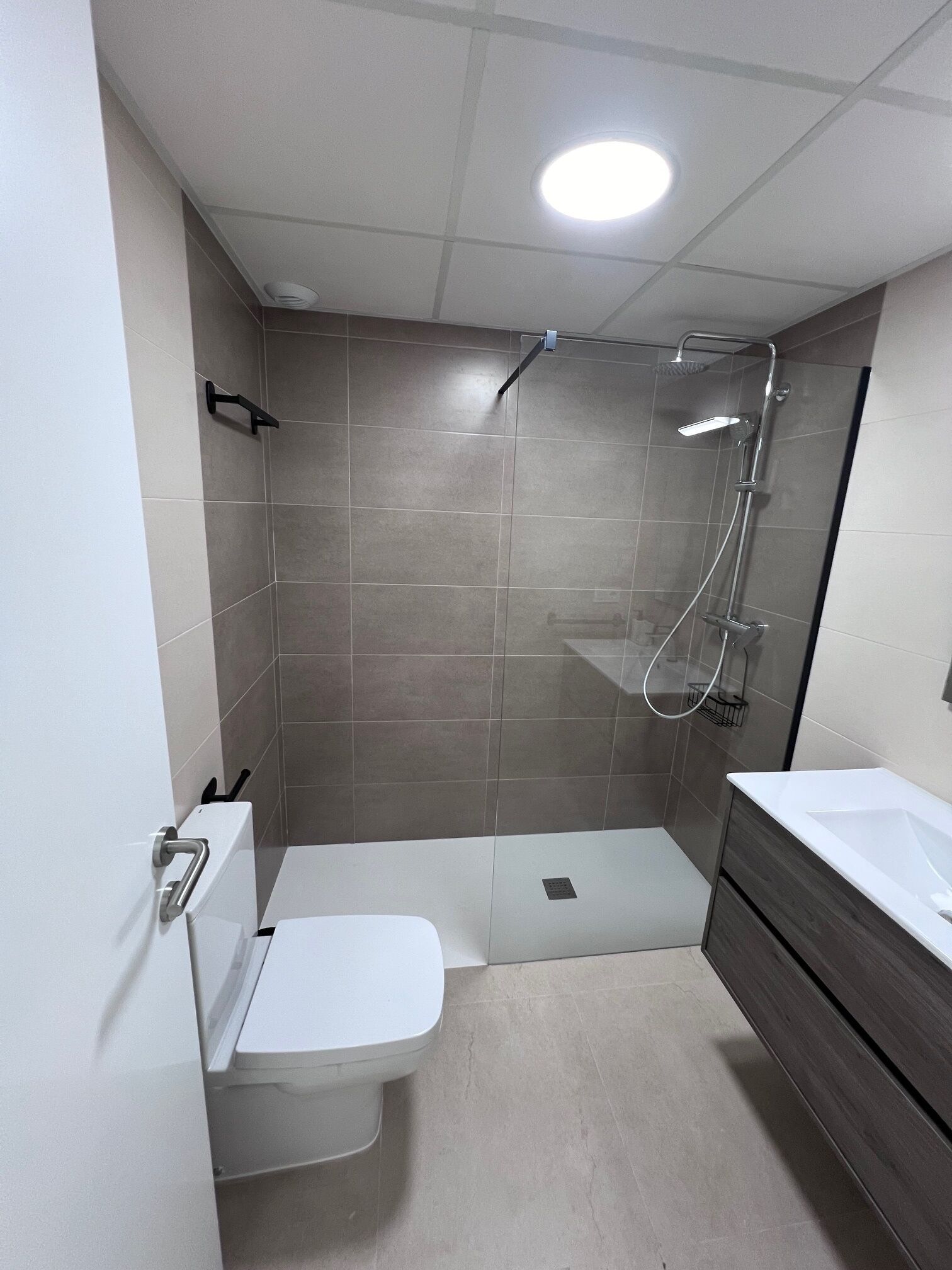Een moderne badkamer met een douche, toilet en wastafel.