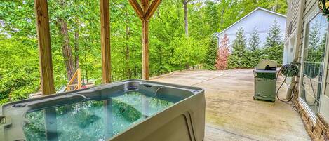 A hot tub under a wooden pergola with a ceiling fan, surrounded by lush greenery.