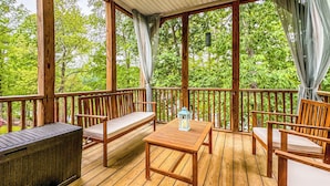 Een houten terras met een bank, tafel en stoelen, omgeven door een houten hekwerk en bomen.