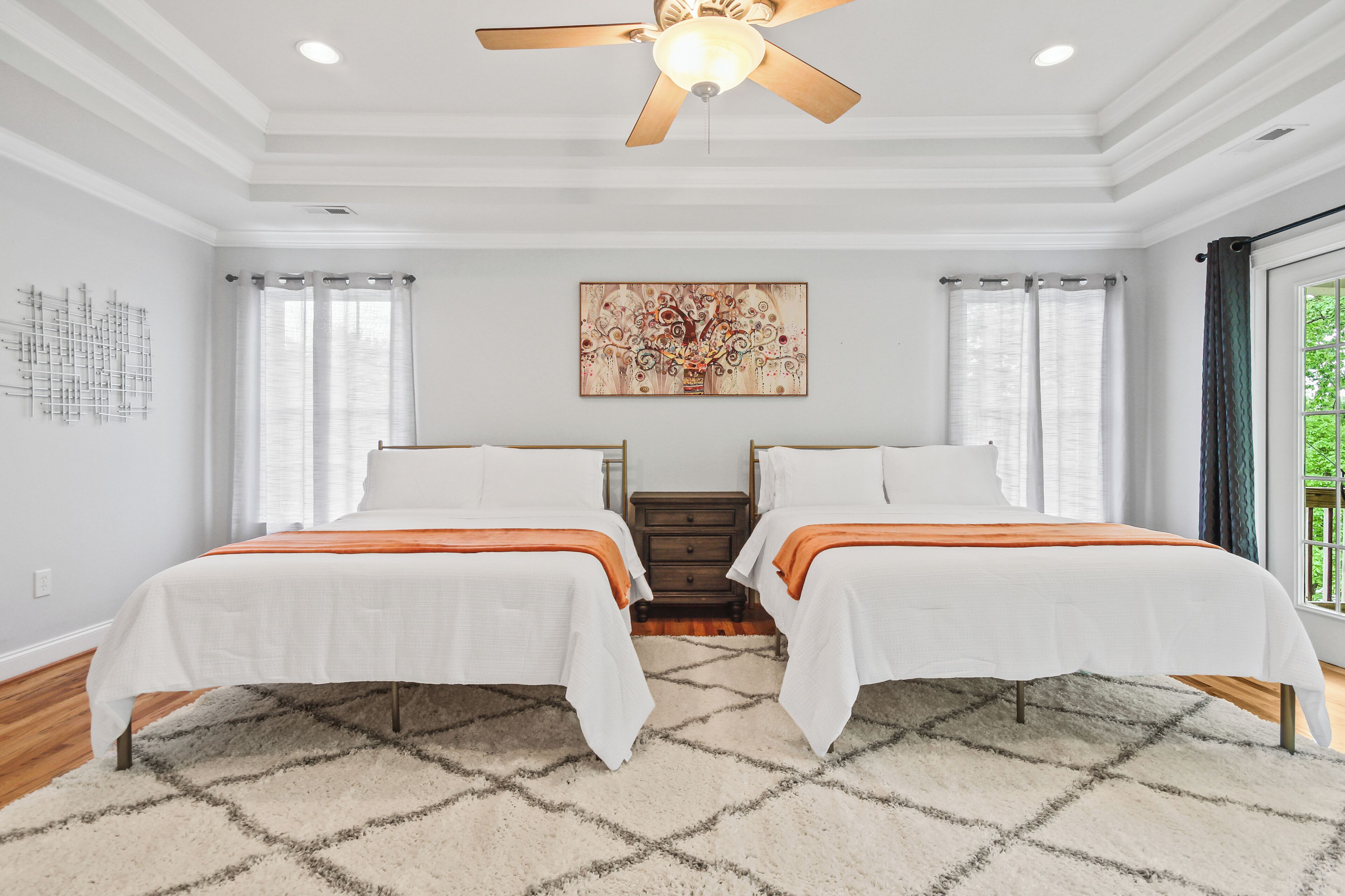 A bedroom with two beds, a ceiling fan, a rug, and a painting on the wall.