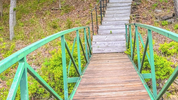 Een houten trap met groene leuningen die naar een huis leidt, omringd door bomen.