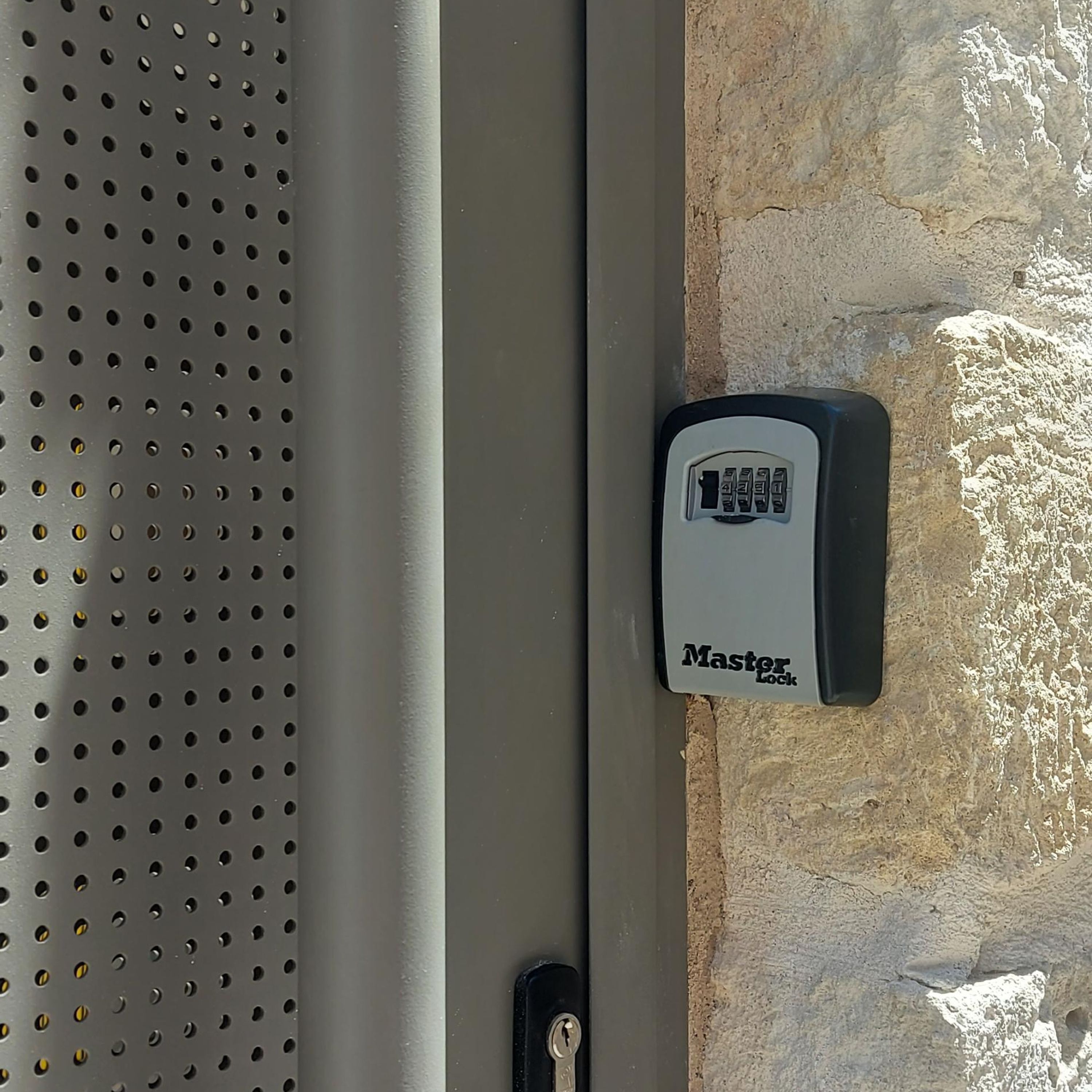 Ein Master Lock Vorhängeschloss auf einer Metalloberfläche mit einem gelochten Muster.