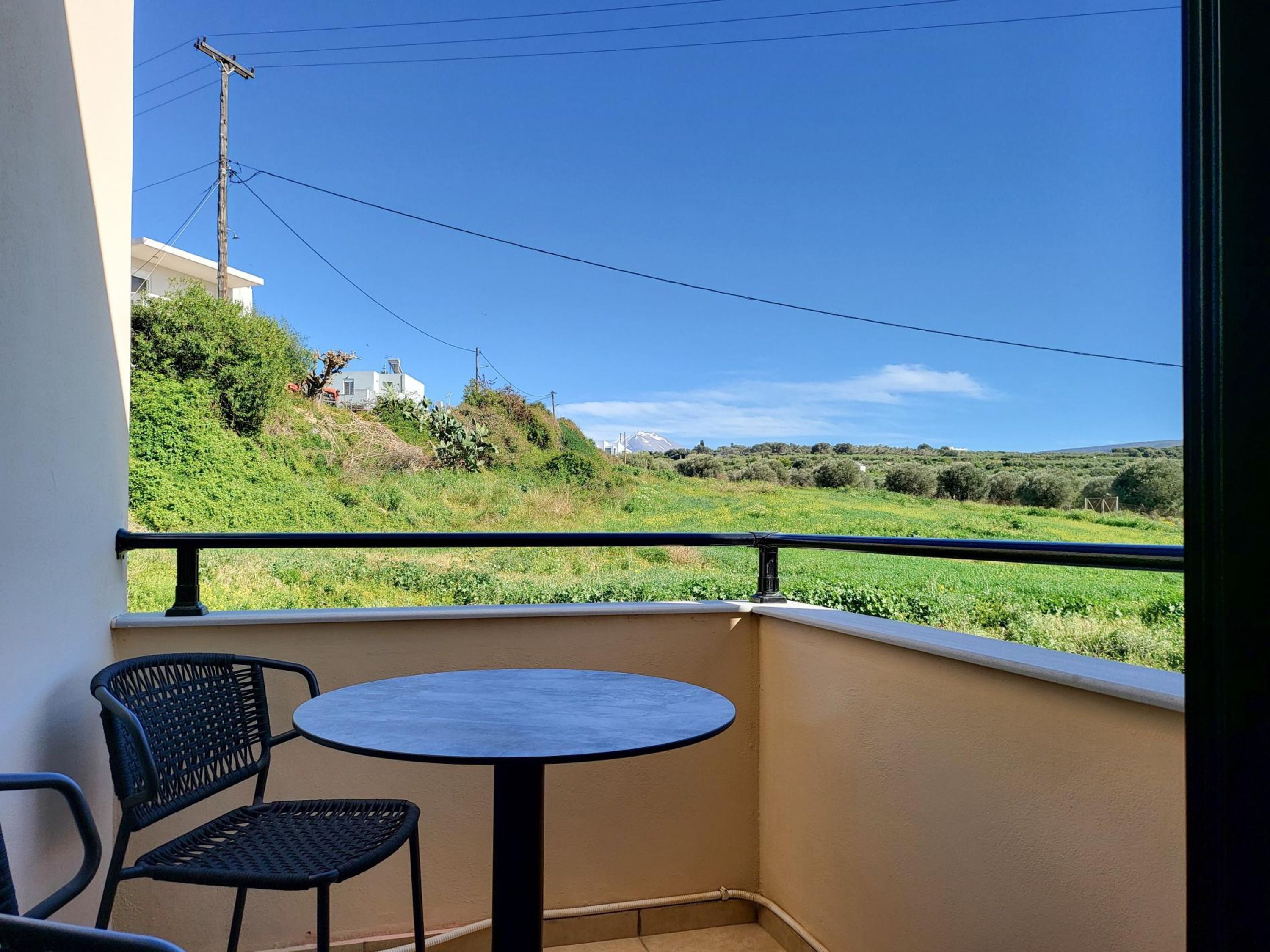 Ein Balkon mit Tisch und Stühlen, der auf eine grüne Landschaft mit Gebäuden und einem Berg im Hintergrund blickt.