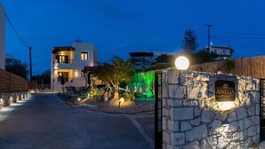 Entrada de uma villa com muro de pedra, uma placa e um caminho que leva a um edifício.