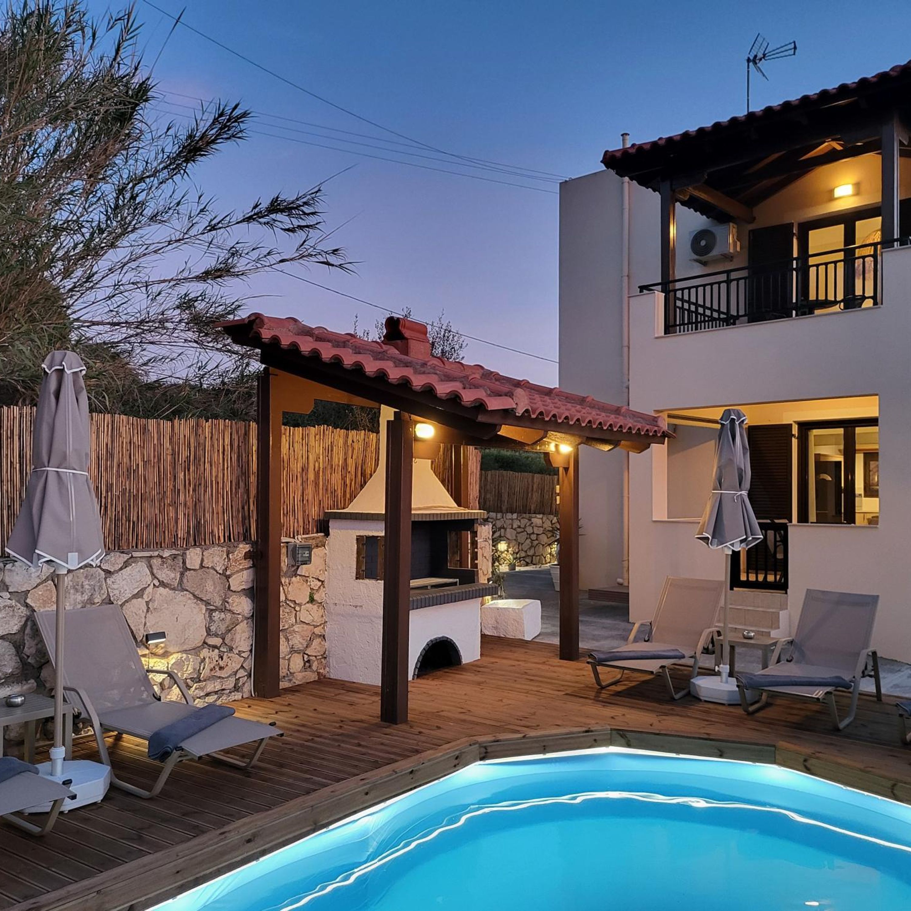 Area piscina con barbecue, poltrone relax e parete in pietra.