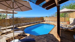 Um deck de madeira com piscina, espreguiçadeiras e guarda-sóis.