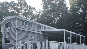 A two-story house with a porch, a stone foundation, and a small garden with pink flowers and an American flag.
