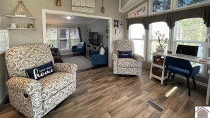 A spacious living area with patterned sofas, a dining table, and a laptop on a desk.