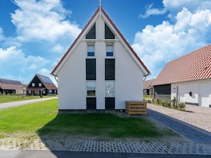 A white single-story house with a red roof, a small front yard, and a paved driveway.