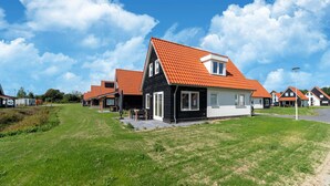 Een rij moderne huizen met oranje daken en een grasveld ervoor.