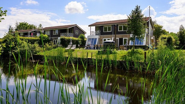 A residential area with houses along a canal, featuring a grassy area and a small body of water. - House in Vlagtwedde With Sauna and Hot Tub (Vlagtwedde)