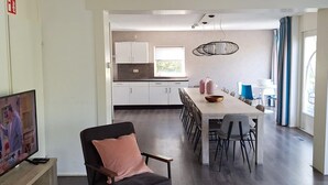 A modern kitchen with white cabinets, a dining area with a long table and chairs, and a television on a wooden stand. - House in Vlagtwedde With Sauna and Hot Tub (Vlagtwedde)