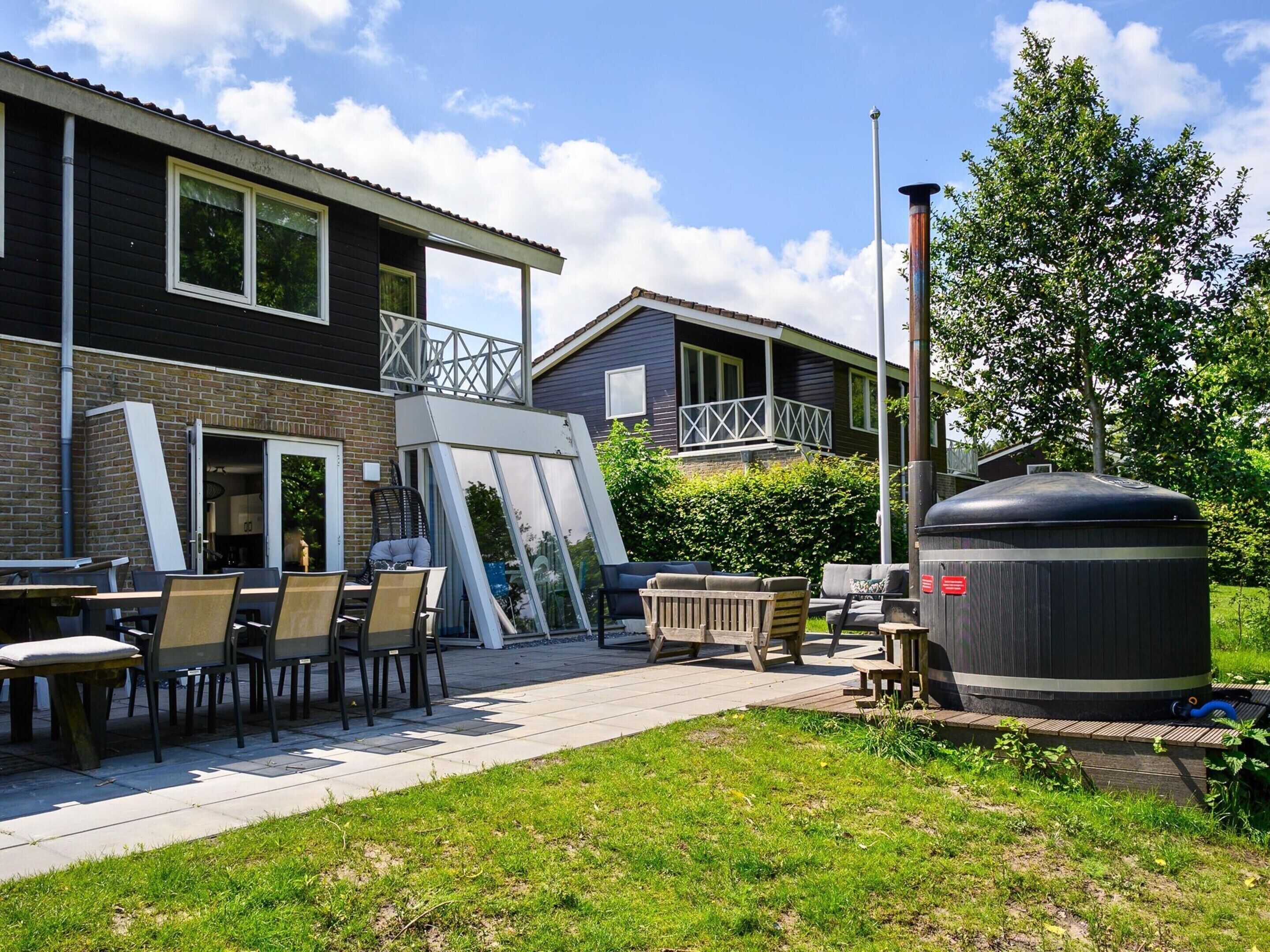 En terrasse med udendørs møbler, en stor vandvarmervandvarmertank og en murstensbygning med balkon.