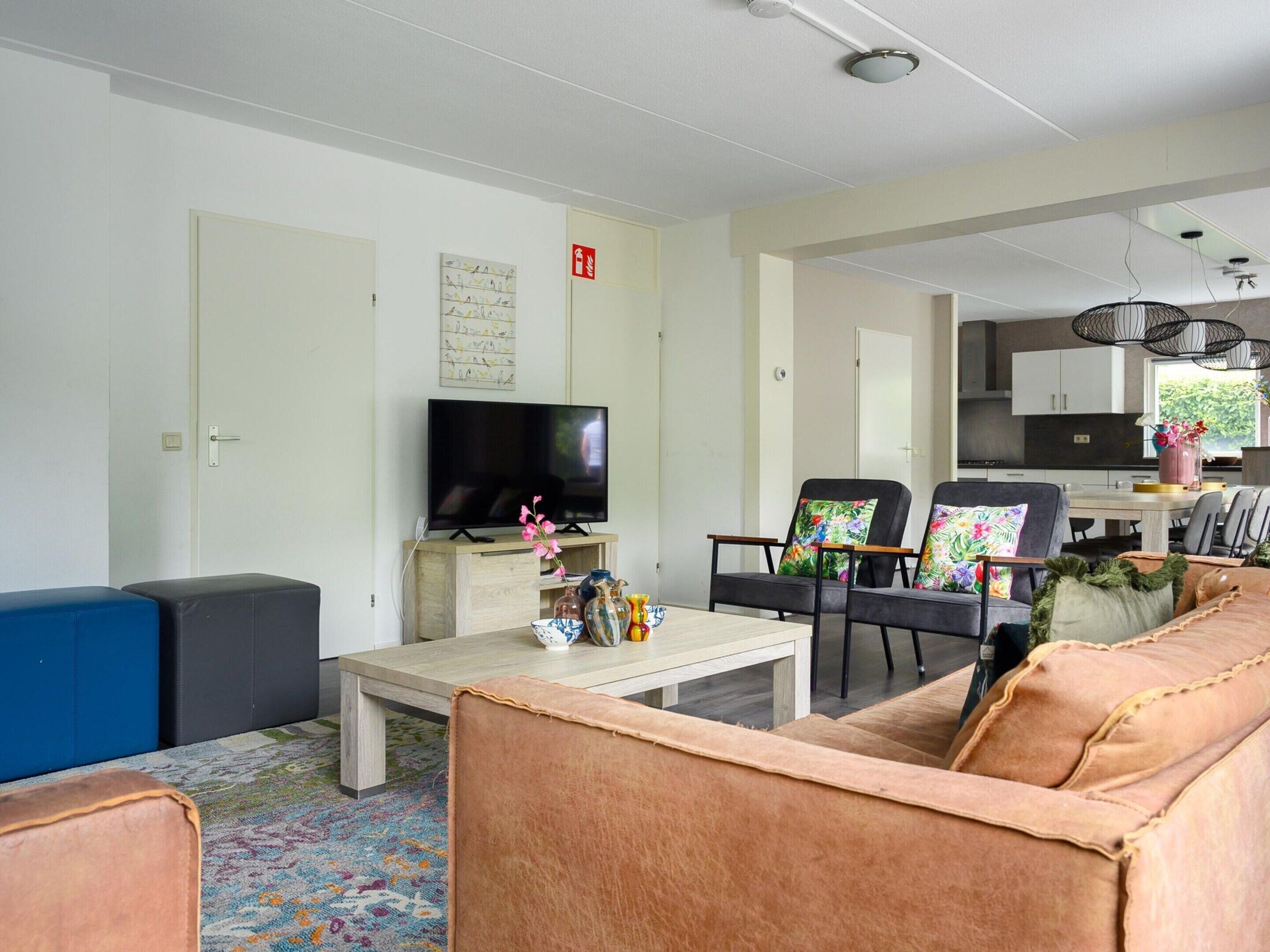 A modern living room with a flat-screen TV, two sofas, a coffee table, and a dining area with chairs and a table.