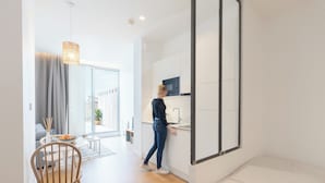 A modern kitchen with a built-in microwave, a dining area with a wooden chair and a small table, and a large window providing natural light. - Les Appartements de Babel Vieux Port (Marseille)