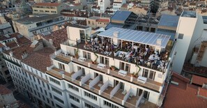 Eine Dachterrasse mit mehreren Ebenen, Sitzbereichen und Essplätzen, umgeben von städtischen Gebäuden.