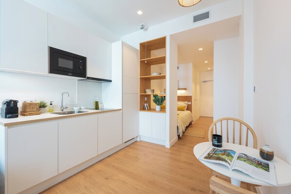 Une cuisine moderne avec des meubles blancs, un four à micro-ondes et un évier. On y trouve également un coin repas avec une table, des chaises et un magazine.
