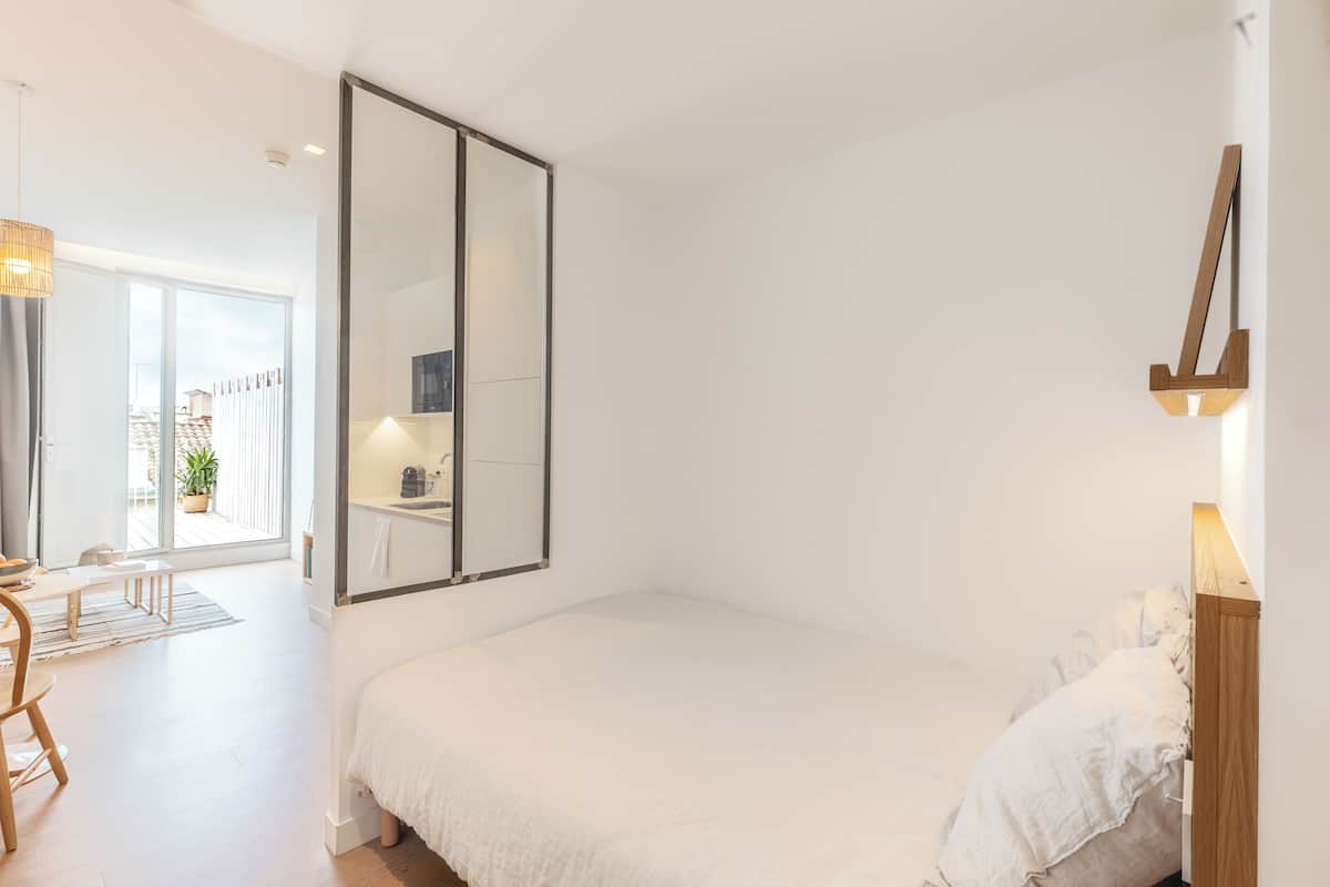 Une chambre avec un grand lit, une table de chevet en bois, un miroir et une vue sur l’extérieur.
