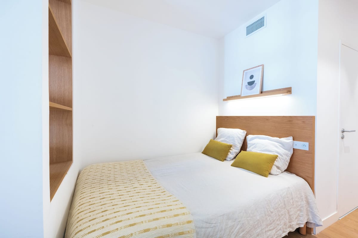Une chambre à coucher bien rangée, avec un lit, une étagère sur laquelle est posée une photo et une porte.