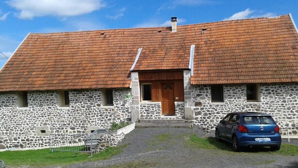 A stone building with a red-tiled roof, a wooden door, and a blue car parked in front. - Aux Portes des Volcans D'auvergne, de la Rivière Dordogne et de ses Barrages (Champagnac)