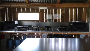A kitchen with stainless steel countertops, a gas stove, a grill, and a window with vertical blinds. - Aux Portes des Volcans D'auvergne, de la Rivière Dordogne et de ses Barrages (Champagnac)
