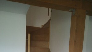 A wooden staircase with a handrail, leading to a landing with a light switch. - Aux Portes des Volcans D'auvergne, de la Rivière Dordogne et de ses Barrages (Champagnac)