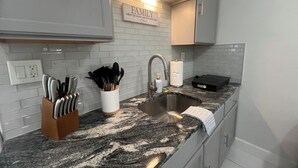 Una cocina moderna con encimera de granito, pileta de acero inoxidable y muebles blancos. Se observa un bloque de cuchillos, un especiero y una toalla de cocina colgada sobre la encimera.