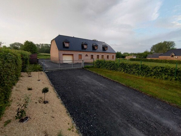 A large brick house with a garage, surrounded by a gravel driveway and a hedge.