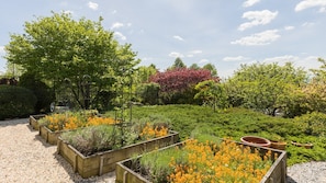 Ein Garten mit erhöhten Blumenbeeten, einer Pergola und verschiedenen Bäumen.