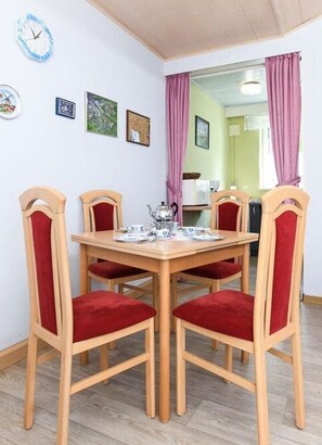 A dining area with a wooden table and six chairs, each with a red cushion. There are wall clocks and framed pictures on the wall. - Holiday Home Roseneck (Esens)