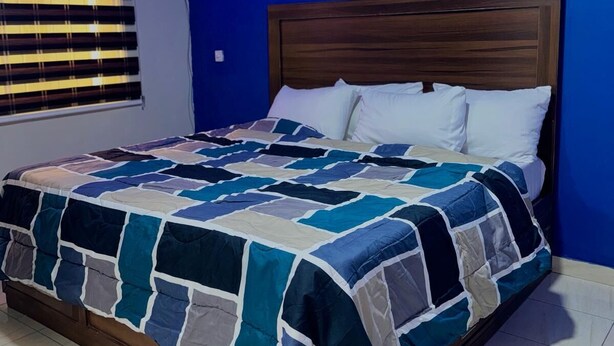 Un dormitorio con cabecera de madera, colcha acolchada y ventana con persianas.