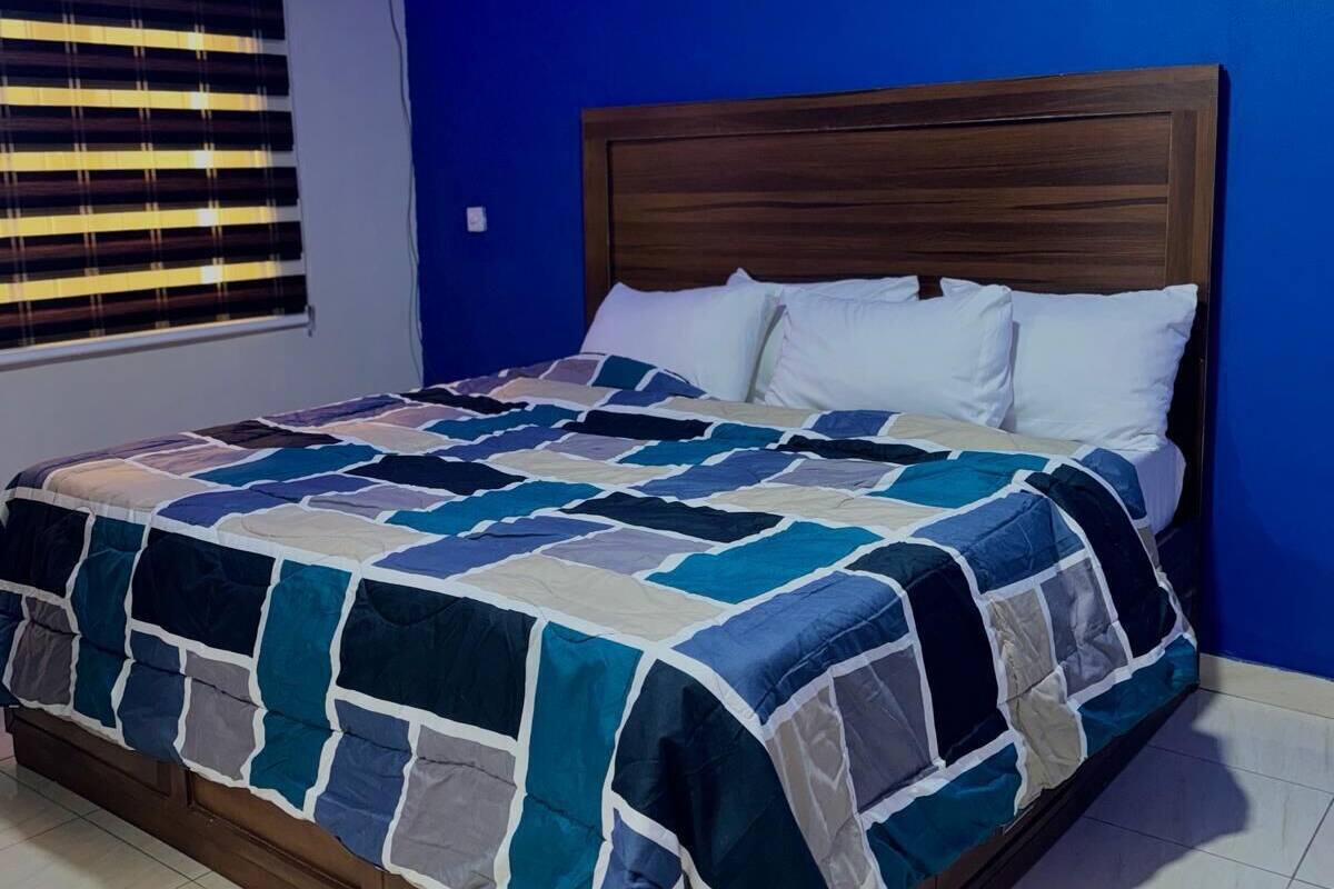A bedroom with a wooden headboard, a quilted bedspread, and a window with blinds.
