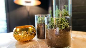 Um terrário de vidro com plantas verdes, uma tigela dourada decorativa e um castiçal de vidro sobre uma superfície de madeira.