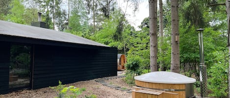 Een chalet met houten buitenkant, een jacuzzi en een terras, omgeven door bomen.