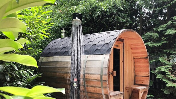 Eine holzverkleidete, fassförmige Struktur mit einer kleinen Veranda und einem Wasserfall.