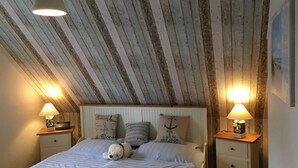 A bedroom with a wooden ceiling, a bed with white bedding, two bedside tables with lamps, and decorative pillows. - Dat Onnen's Hus - Burhave 3 (Butjadingen)