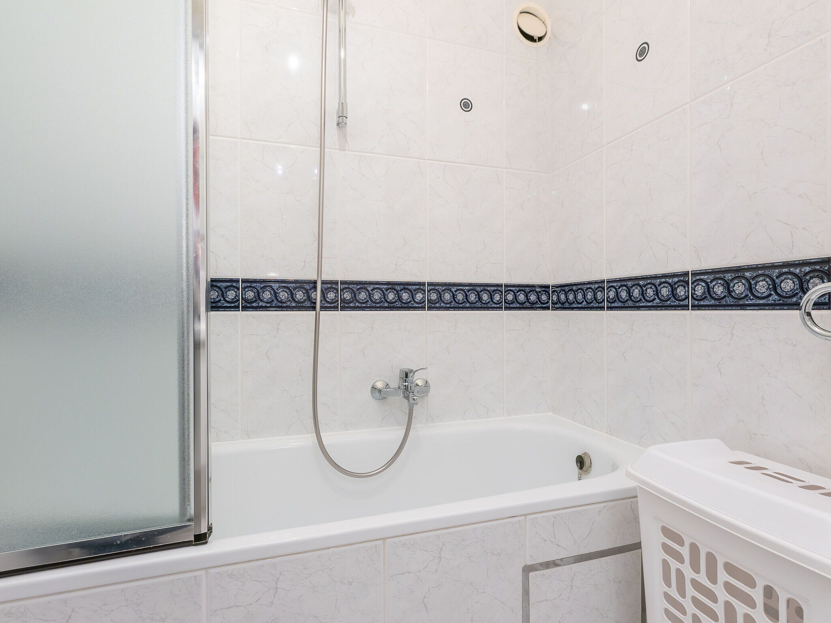A bathroom with a glass shower enclosure, a white bathtub, and a white laundry basket.