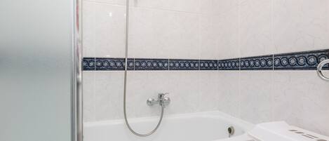 A bathroom with a glass shower enclosure, a white bathtub, and a white laundry basket.