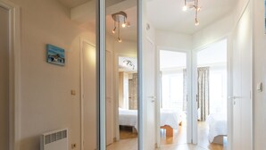 Un couloir d’hôtel moderne avec un mur miroir, un radiateur et un lit dans la chambre adjacente.