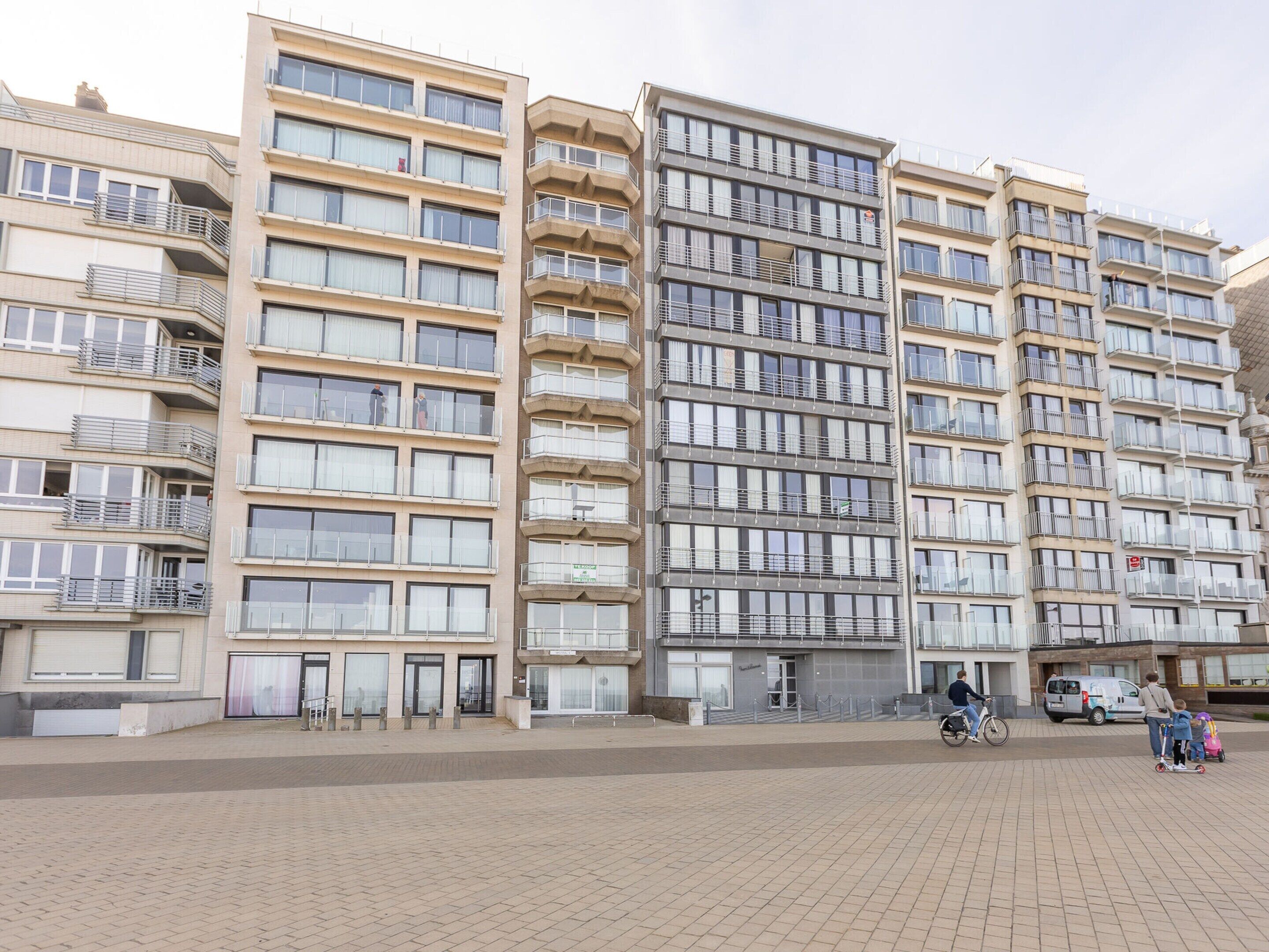 Een meerlaags woongebouw met balkons, een verhard begane grond en een heldere lucht.