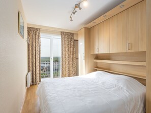 A bedroom with a large bed, wooden wardrobe, and a view through a window. - Apartment With 2 Bedrooms and sea View (Middelkerke)