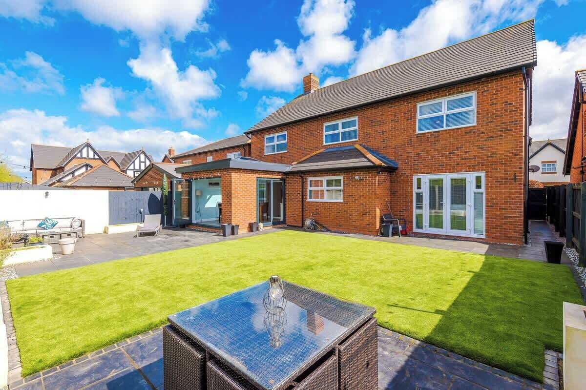 A residential property with a well-maintained lawn, a patio area with a glass-top table, and a brick house with a garage.