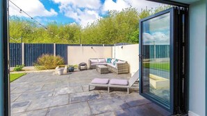 Un espace extérieur aménagé en terrasse, avec des sièges et une porte vitrée donnant sur un jardin.