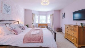 Une chambre à coucher avec un lit, une commode, un téléviseur et une fenêtre avec des rideaux.